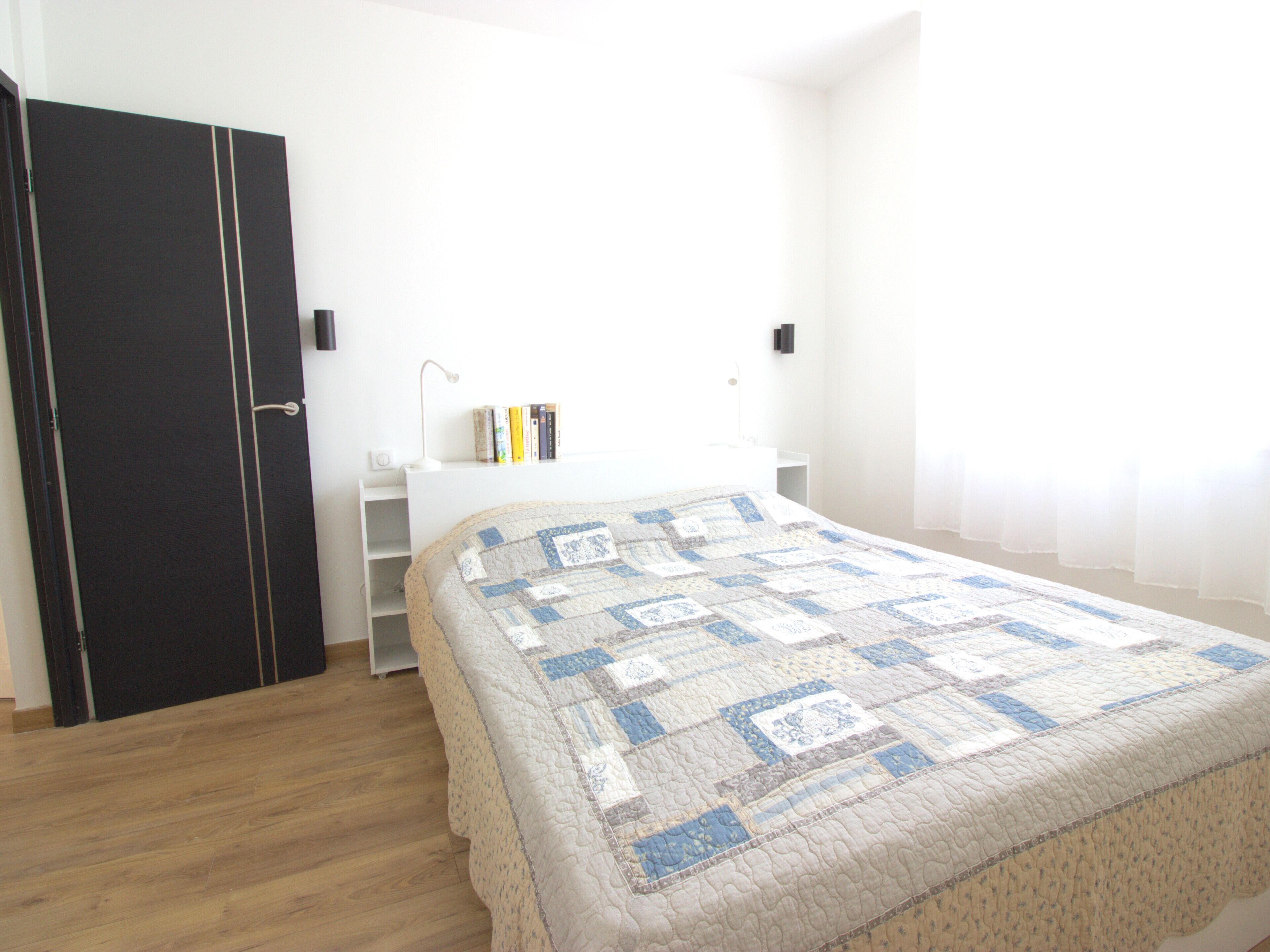 A bedroom with a bed, a nightstand, a bookshelf, and a wardrobe.