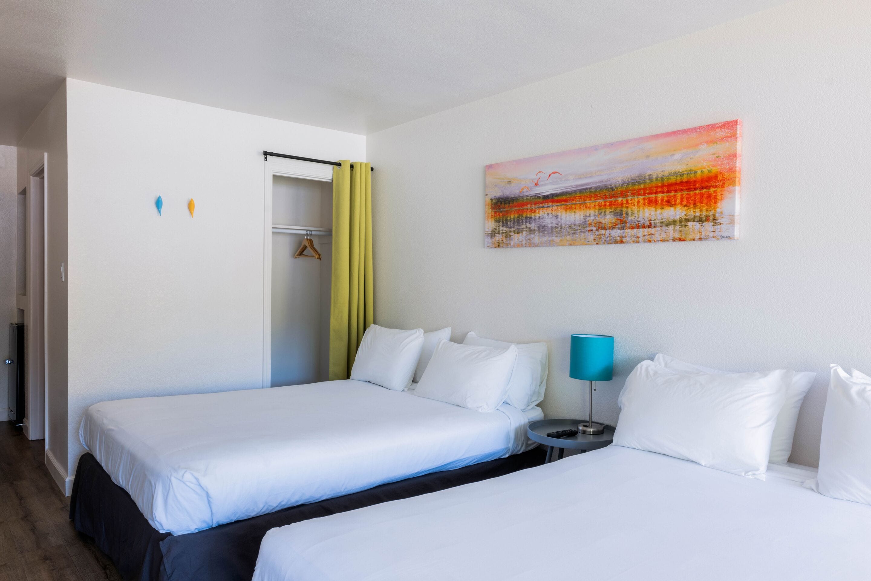 A hotel room with two beds, a painting on the wall, and a small table with a lamp.