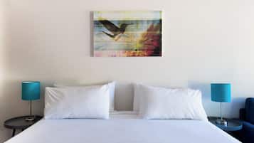 Habitación de hotel con una cama, dos almohadas blancas, un cuadro de un pájaro colgado en la pared y dos lámparas de noche.
