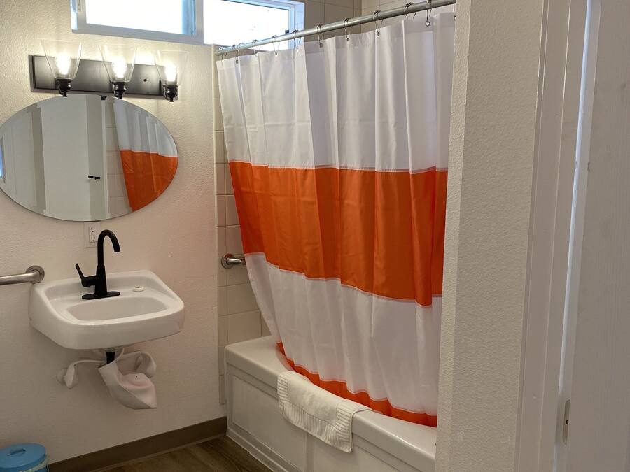 A bathroom with a white sink, a mirror, a shower curtain, and a blue trash can.