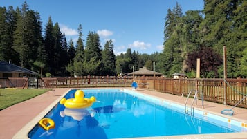 A rectangular swimming pool with a blue interior, surrounded by a wooden fence, and a grassy area with trees in the background.
