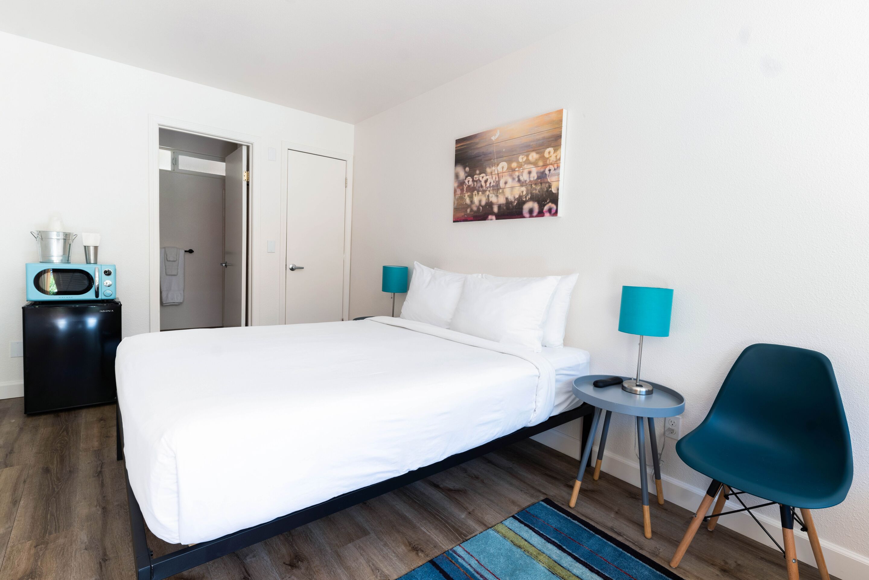 A neatly arranged hotel room with a large bed, a small side table, a chair, a microwave, and a door leading to another room.