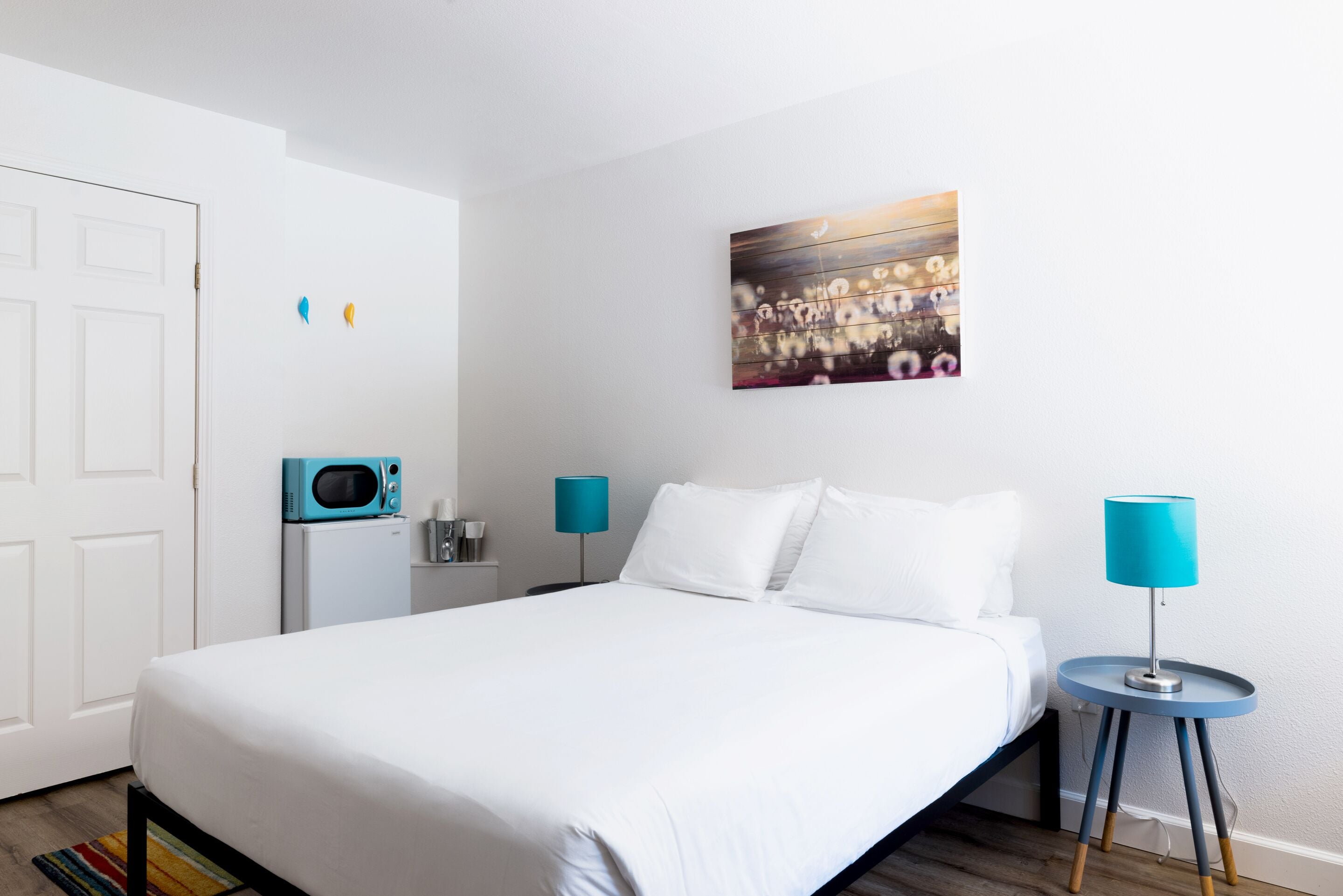 Habitación de hotel ordenada con cama, un cuadro en la pared, microondas y dos lámparas.