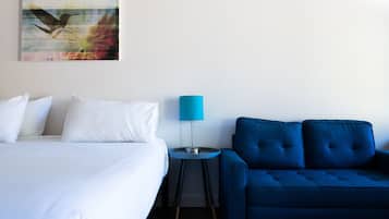 Ein Hotelzimmer mit einem Bett, einem blauen Sofa, einem kleinen runden Tisch mit einer Lampe und einem an der Wand hängenden Kunstwerk.