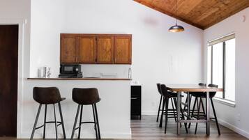 A modern kitchen with wooden cabinets, a bar area with stools, and a dining table with chairs.