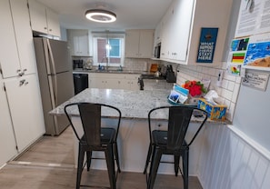Een moderne keuken met twee barkrukken, een roestvrijstalen koelkast en een granieten aanrecht.