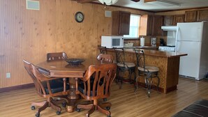 Cucina con rivestimenti in legno, un tavolo da pranzo con sedie, una ventola a soffitto e un frigorifero.
