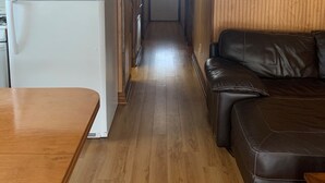 Un corridoio stretto con pareti in legno e un frigorifero bianco sulla sinistra. Un divano in pelle marrone si trova sulla destra.