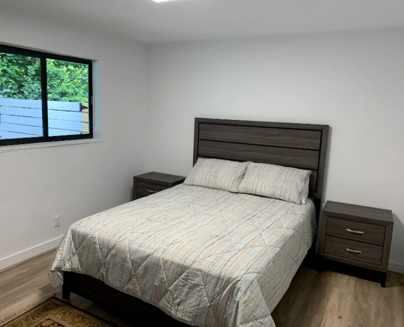 Un dormitorio con cama, dos mesitas de noche, una ventana y vistas a zonas verdes.