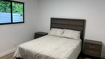 Un dormitorio con cama, dos mesitas de noche, una ventana y vistas a zonas verdes.
