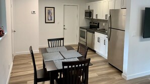 A compact kitchen with white cabinets, a stainless steel refrigerator, a microwave, and an oven. There is a dining table with chairs and a framed picture on the wall. - Fort Lauderdale Beach Flats #6 - Centrally Located! (Fort Lauderdale)