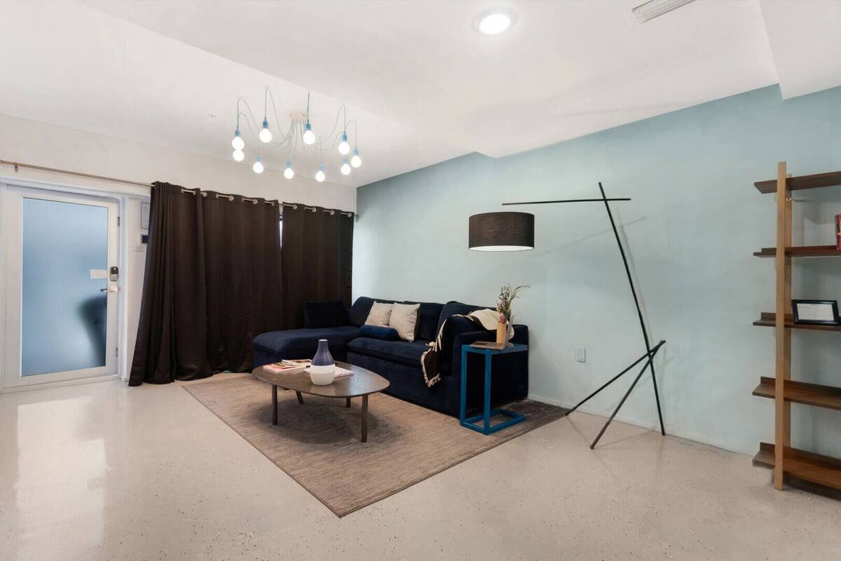 Een moderne woonkamer met een donkerblauwe bank, een salontafel, een vloerlamp en een boekenkast.