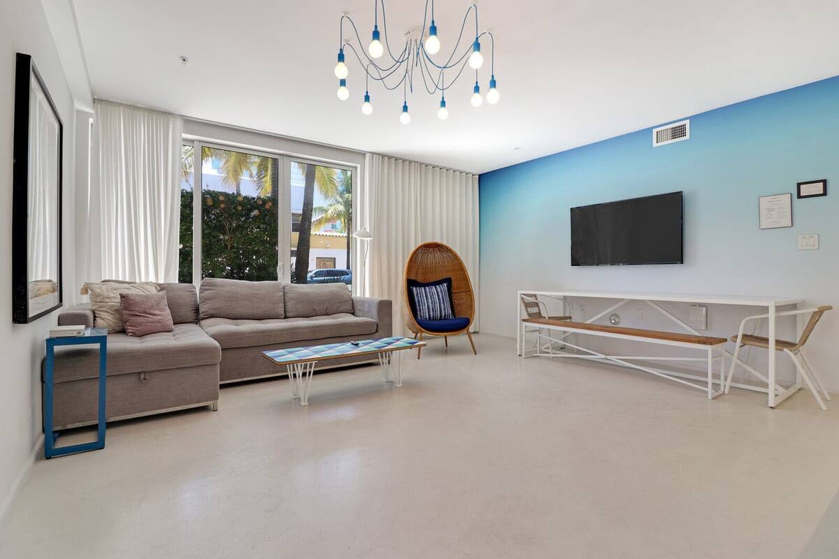 Een moderne woonkamer met een bank, een salontafel, een rieten fauteuil, een televisie en een wit bureau.