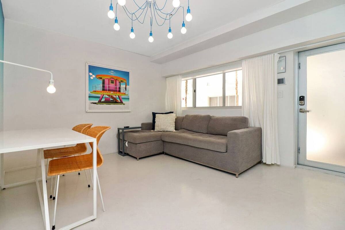 Een moderne woonkamer met een witte tafel, twee oranje fauteuils, een grijze bank en een kleurrijk schilderij aan de muur.