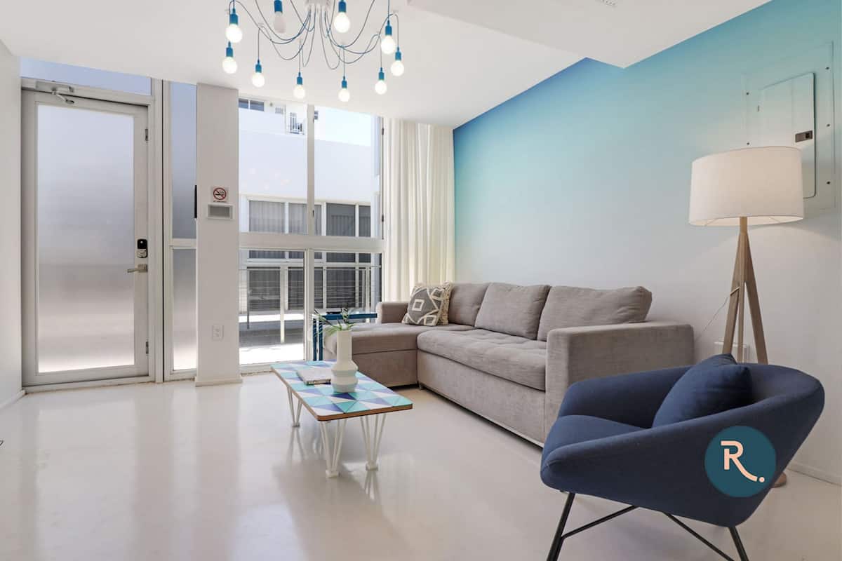 Een moderne woonkamer met een bank, een blauwe fauteuil, een salontafel en een lamp.