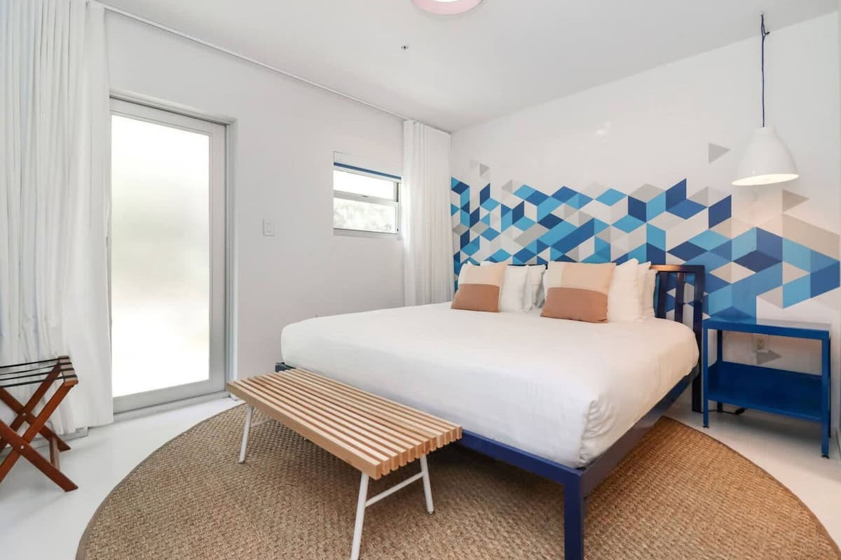 Een moderne hotelkamer met een groot bed, een houten bankje, een blauwe nachtkastje en een wand met een geometrisch patroon.