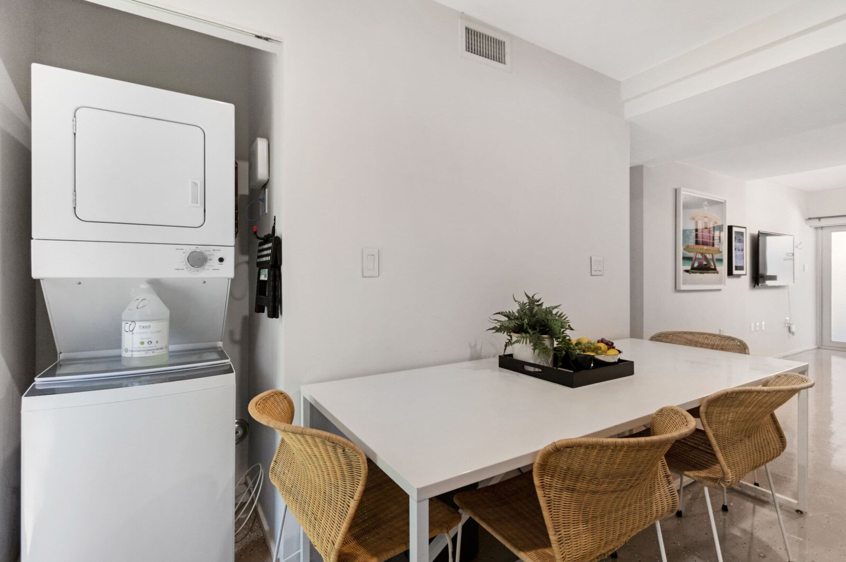 Un comedor moderno con una mesa blanca, sillas de mimbre y una planta como centro de mesa.