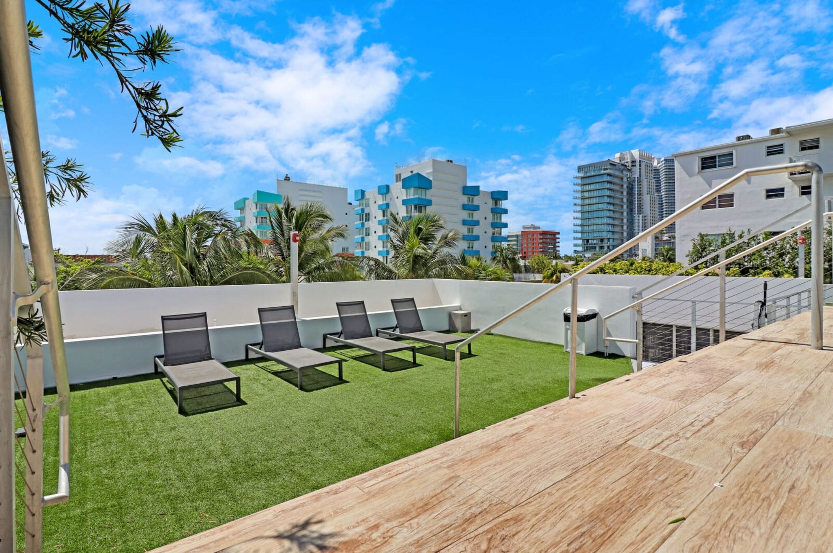 A rooftop terrace with artificial grass, sun loungers, and a view of surrounding buildings.