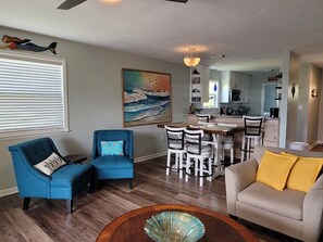 A living room with a dining area, wooden flooring, and a painting of waves. - 2 night minimum! Flexible Booking Dates! (Cape San Blas)