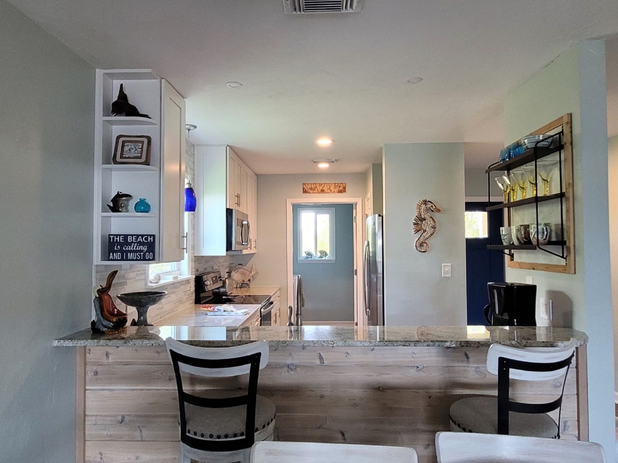A modern kitchen with white cabinets, a marble countertop, and a seahorse decoration on the wall.