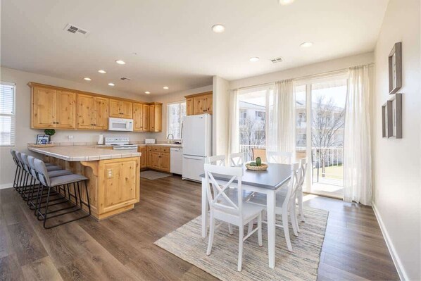 A modern kitchen with wooden cabinets, a central island, and a dining area with white chairs. - Las Palmas Resort #1706 | All-Inclusive Amenities (Saint George)