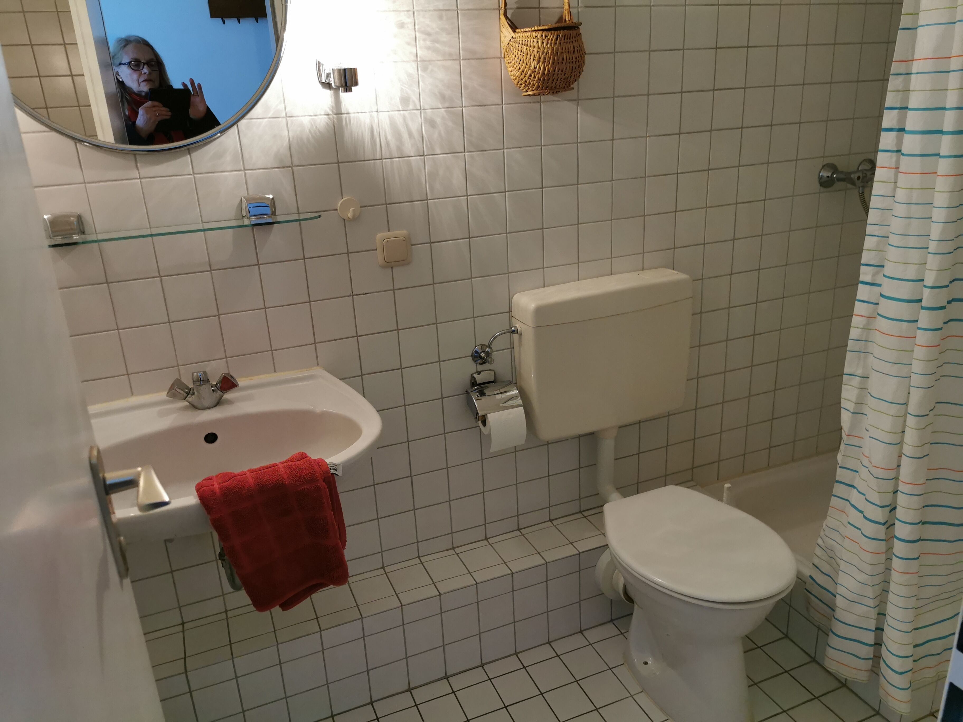 A bathroom with a white sink, toilet, and shower. There is a red towel hanging on the sink.