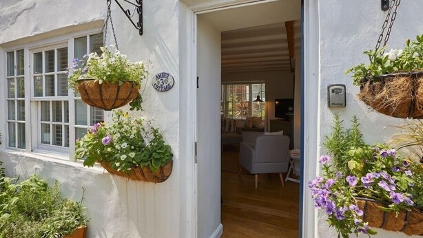 A white cottage with hanging flower baskets and a wooden door. - Amber Cottage (Whitby)