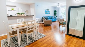Uma sala de estar moderna com uma mesa de jantar de madeira, cadeiras brancas, um sofá azul e uma mesa de centro.