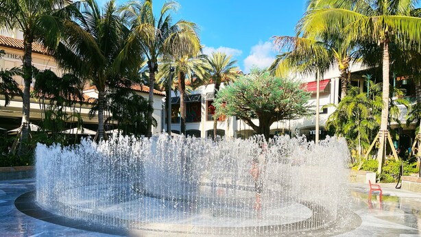 Uma fonte em uma praça com piso de azulejos e uma mesa azul.