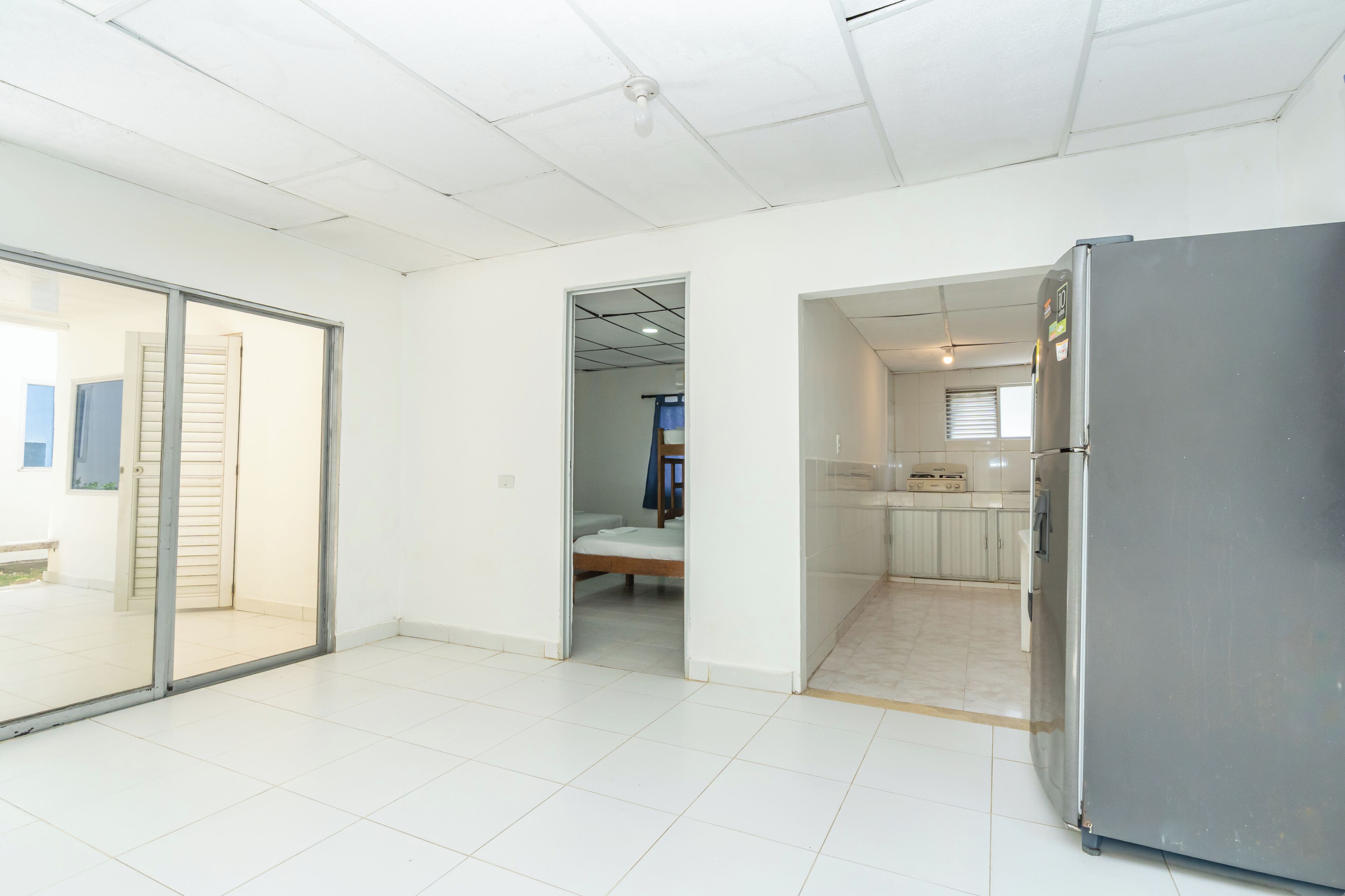 Une pièce spacieuse dotée d’une porte-fenêtre coulissante donnant sur un balcon, d’une kitchenette avec réfrigérateur et d’un lit dans la pièce adjacente.