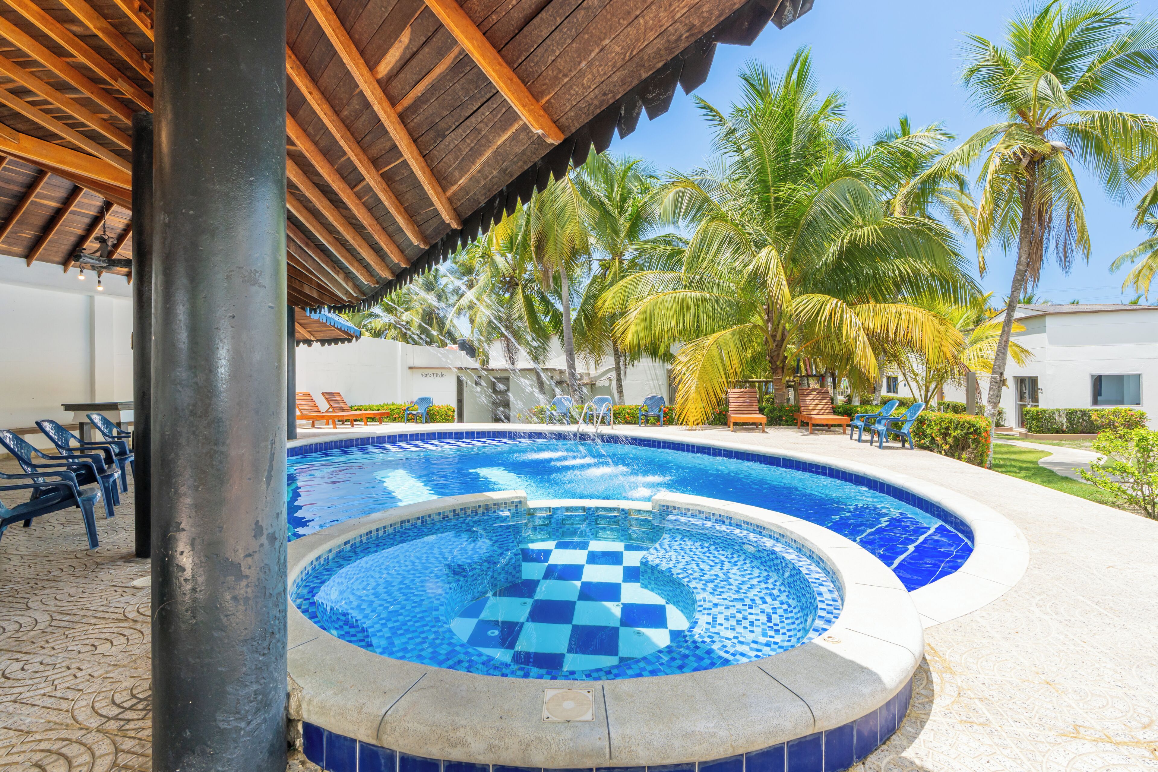 A swimming pool with a checkered pattern, surrounded by palm trees and lounge chairs.