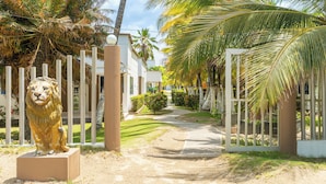 A gated entrance with a lion statue, palm trees, and a pathway leading to a building. - Cabañas La Fragata Coveñas (Coveñas)