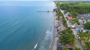 An aerial view of a coastal area with a beach, palm trees, and buildings along the shore. - Cabañas La Fragata Coveñas (Coveñas)
