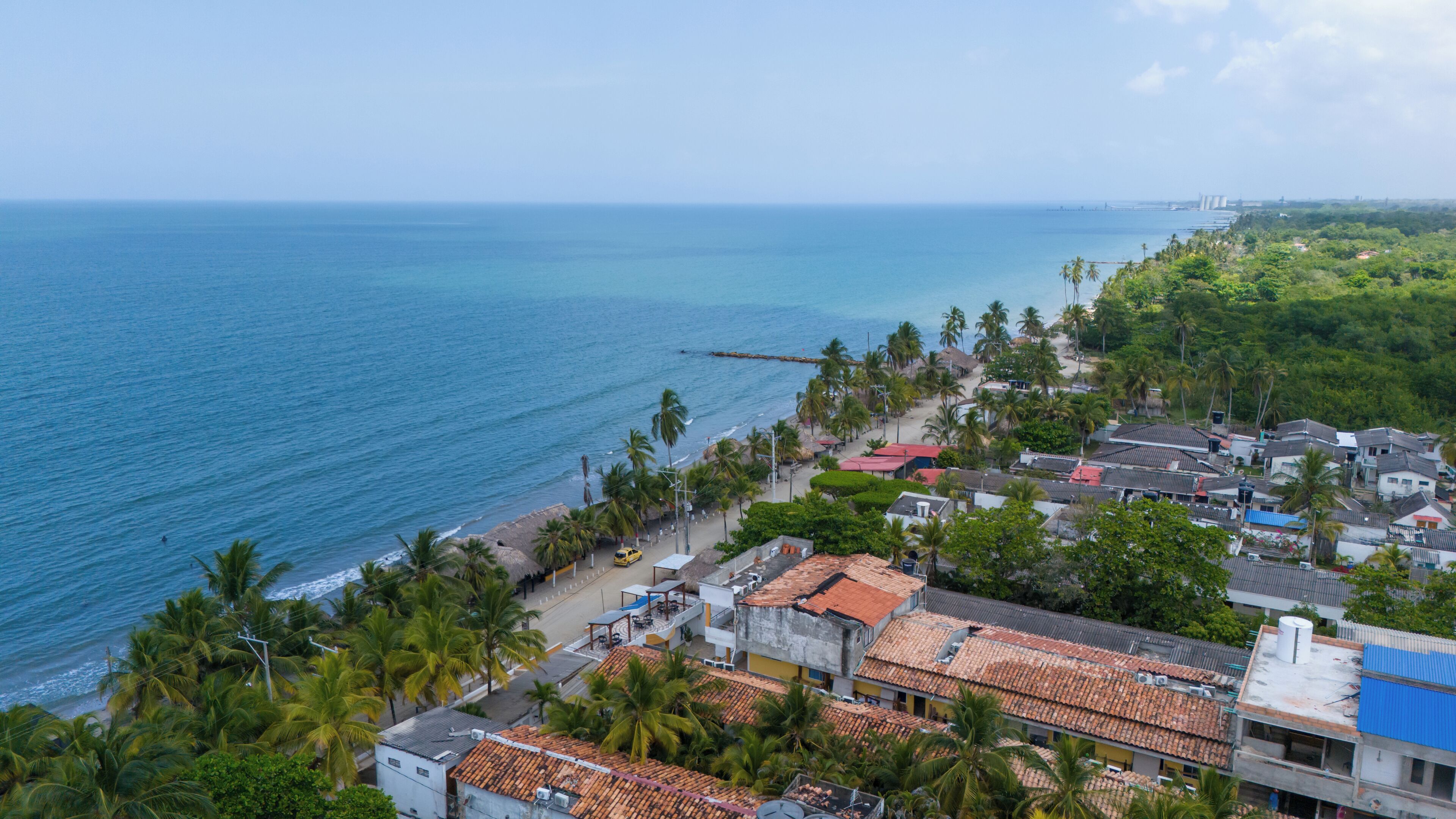 A coastal town with a beach, palm trees, and buildings with red-tiled roofs.
