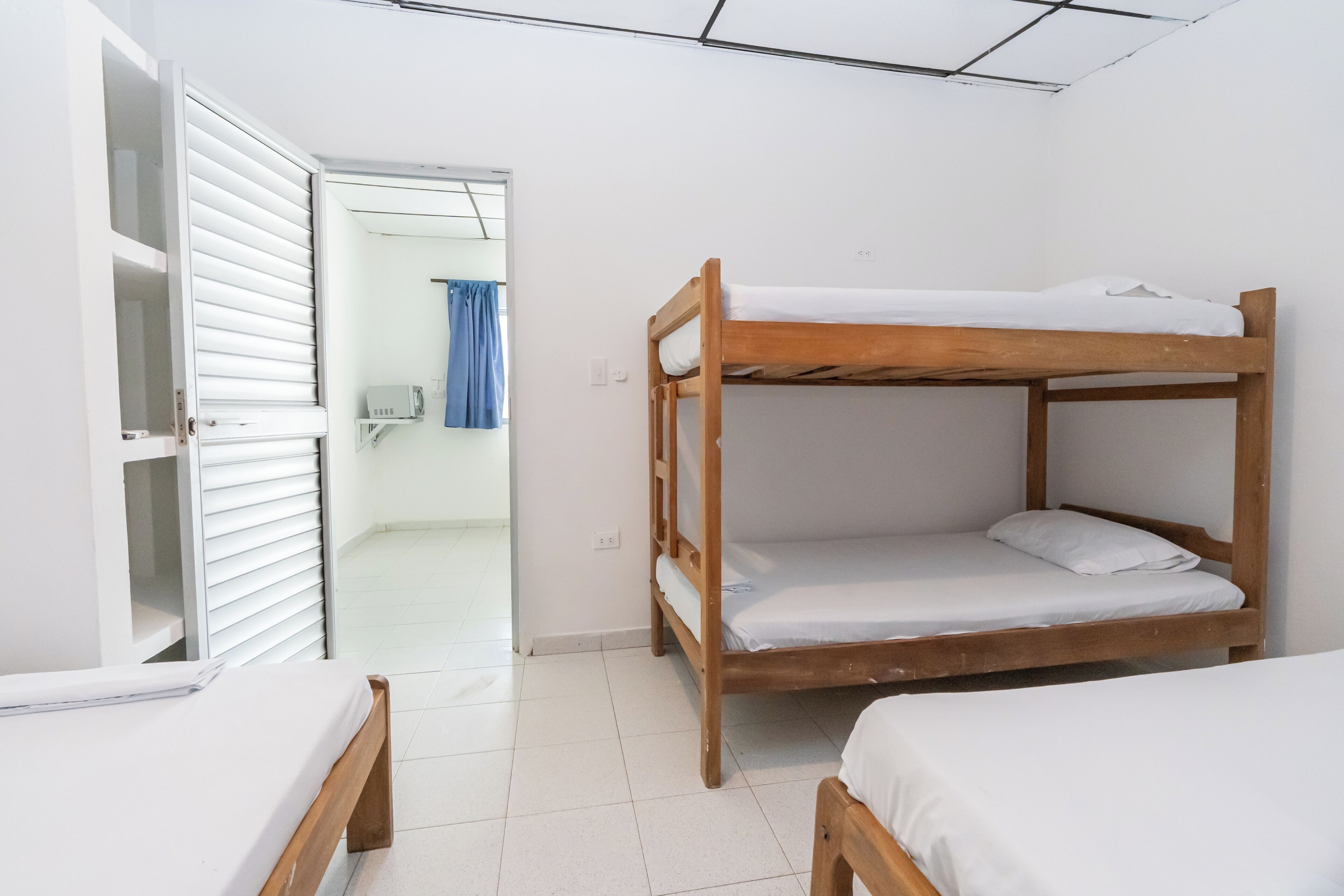 Quarto com duas beliches, um guarda-roupa branco e uma porta para um banheiro.