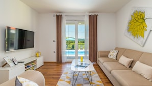 Un salon moderne doté d’un téléviseur à écran plat, d’un canapé, d’une table basse et offrant une vue sur une piscine grâce à de grandes fenêtres.