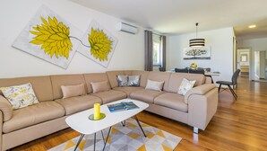 Un salon moderne avec un canapé d’angle beige, une table basse blanche et deux grandes peintures représentant des feuilles jaunes accrochées au mur.
