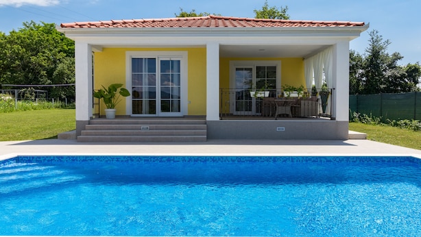 Une maison avec une piscine, un patio couvert et un toit recouvert de tuiles rouges.