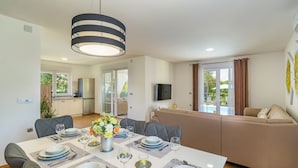 Un espace repas moderne avec une table dressée pour six personnes, un canapé et un téléviseur fixé au mur.