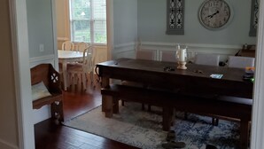 A dining area with a wooden table, benches, and a chandelier. There is a clock on the wall and a window with blinds. - Augusta Golf Course Rental Home MASTERS (Evans)