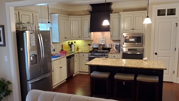 A modern kitchen with white cabinets, stainless steel appliances, a granite countertop, and a bar area with stools. - Augusta Golf Course Rental Home MASTERS (Evans)