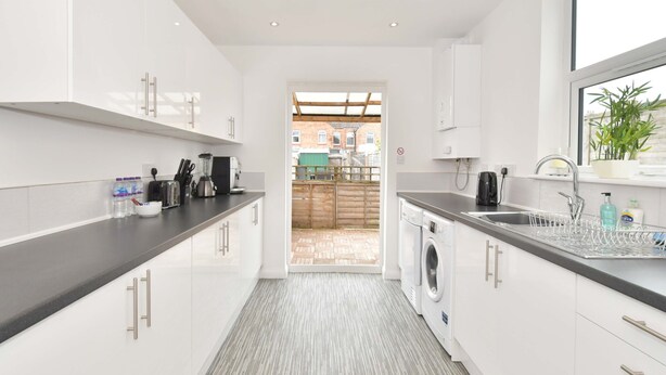 A modern kitchen with white cabinets, a built-in washing machine, and a window with a view of the outside. - Townhouse @ 86 Brooklyn Street Crewe (Crewe)