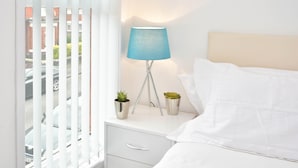 A neatly made bed with white linens, a bedside lamp with a blue shade, and two small potted plants on a white bedside table. - Townhouse @ 86 Brooklyn Street Crewe (Crewe)