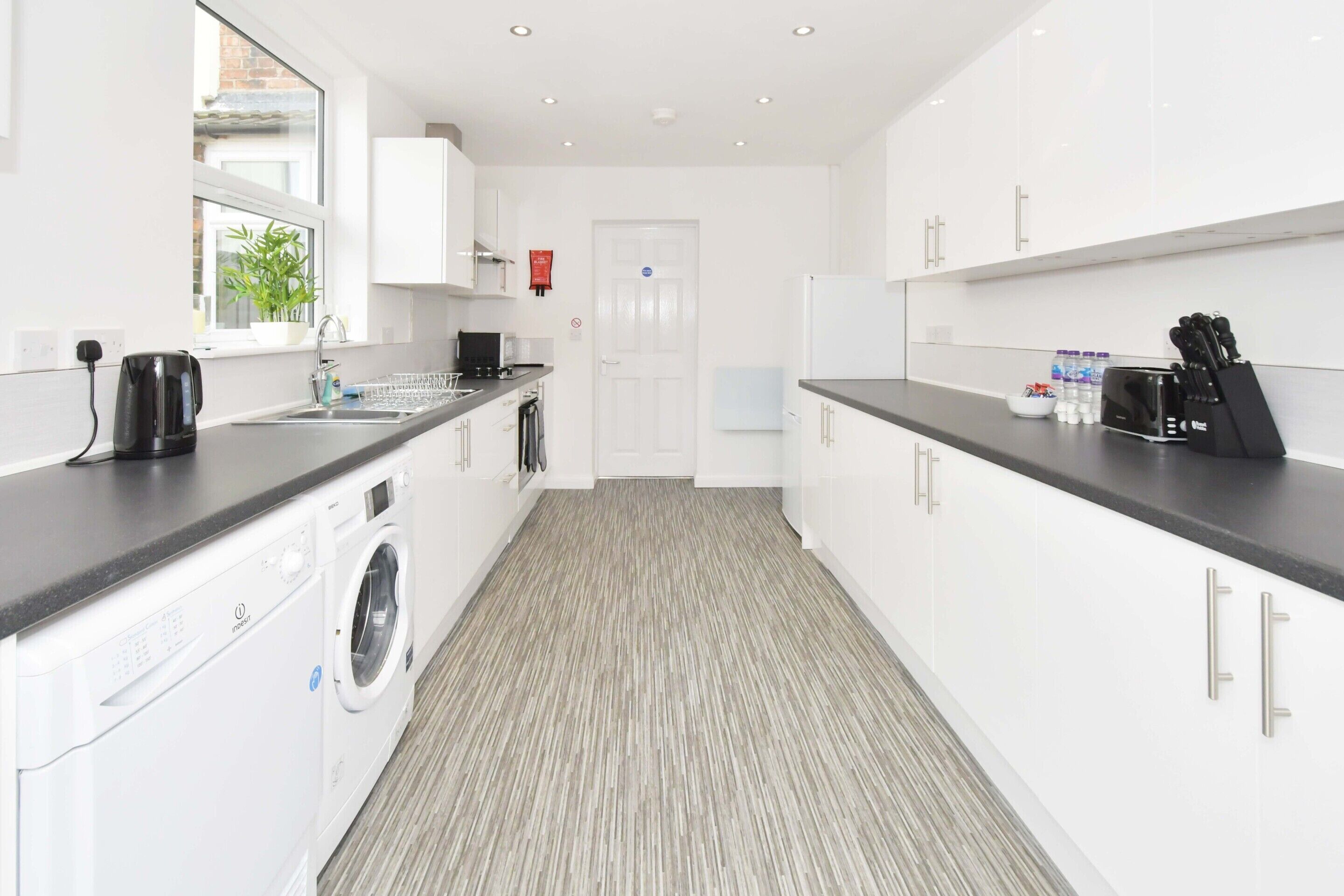 A modern kitchen with white cabinets, a washing machine, and a sink.