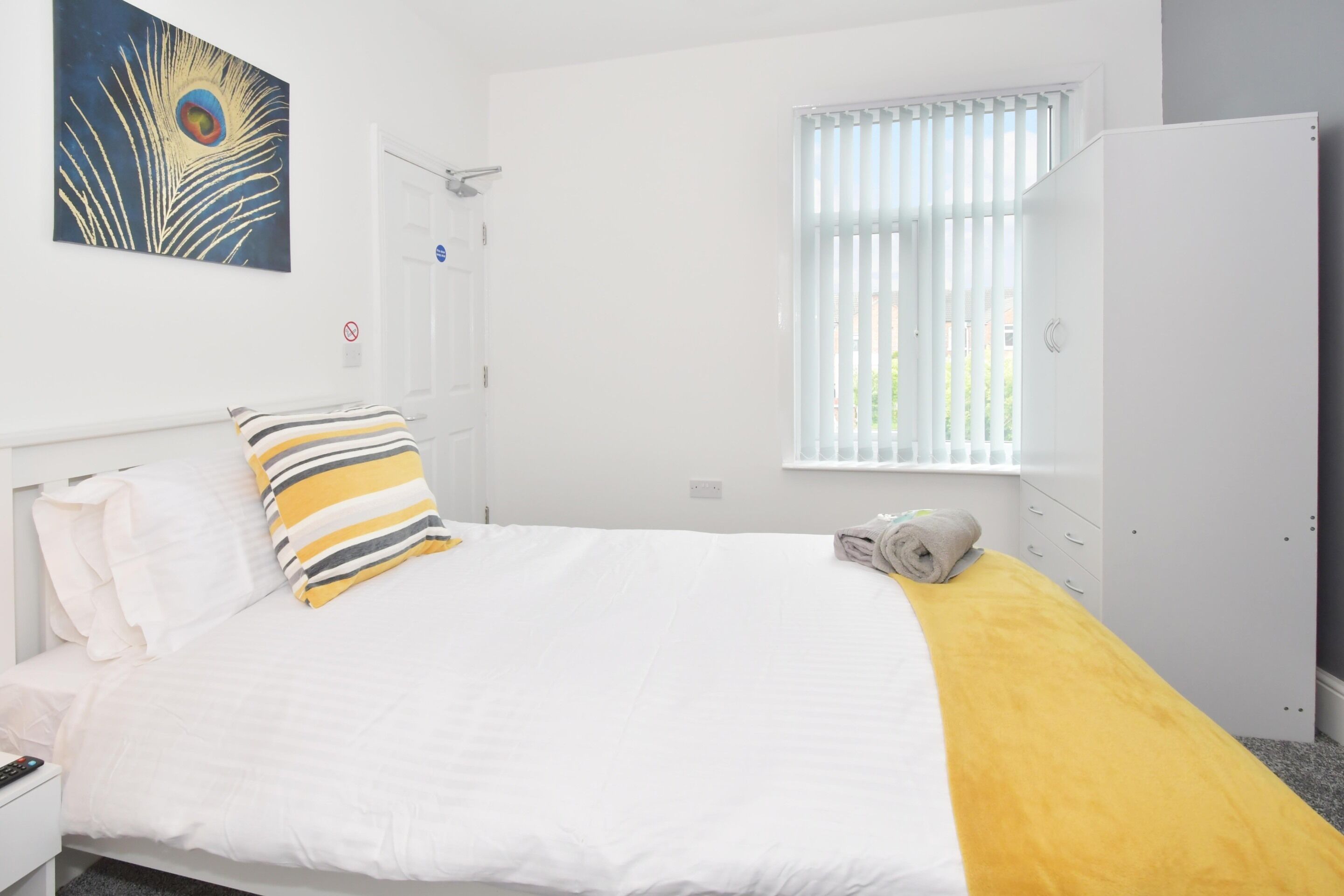 A neatly arranged bedroom with a bed, a nightstand, a wardrobe, and a window with blinds.