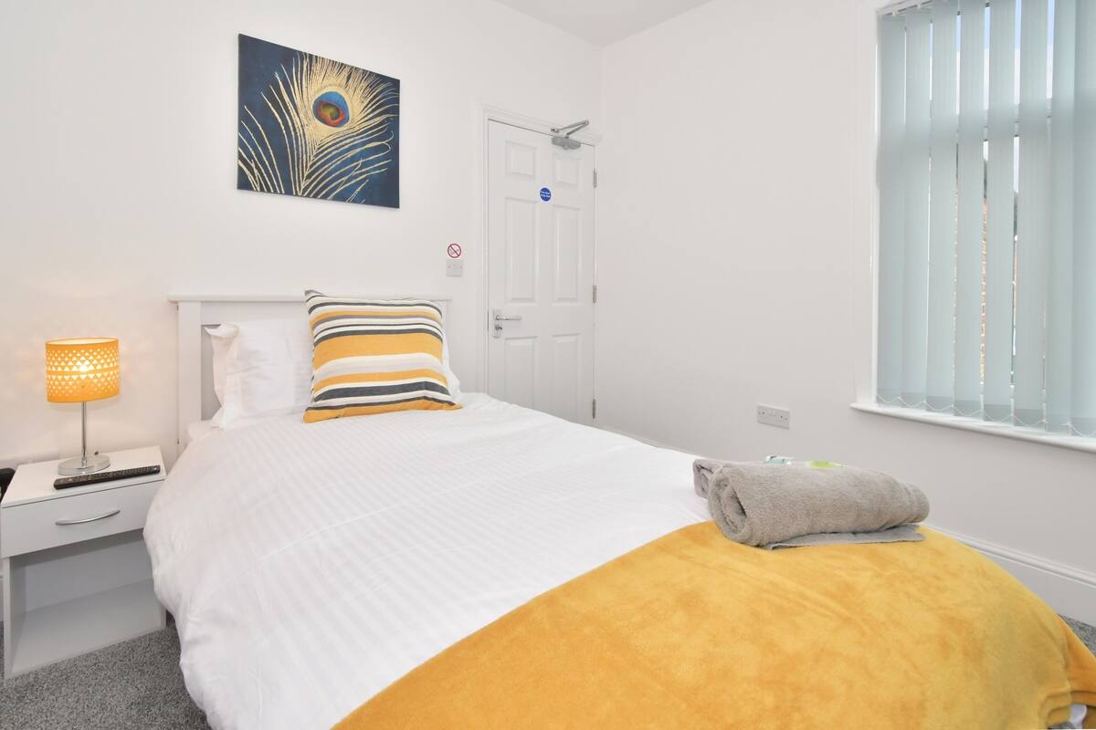 Un dormitorio ordenado con cama, lámpara de noche, toalla y puerta.
