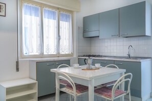 A kitchen with a white table, blue cabinets, and a window with lace curtains.