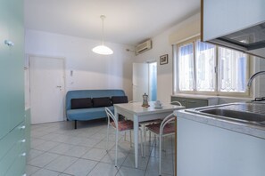 A compact kitchen with a dining table, a blue sofa, and a window with lace curtains.