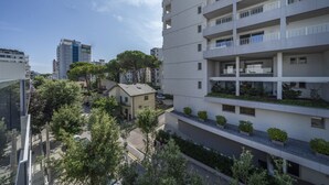 A multi-story residential building with balconies, a parking area, and surrounding greenery.