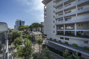Un immeuble résidentiel à plusieurs étages, doté de balcons, d’un espace de stationnement et entouré de verdure.